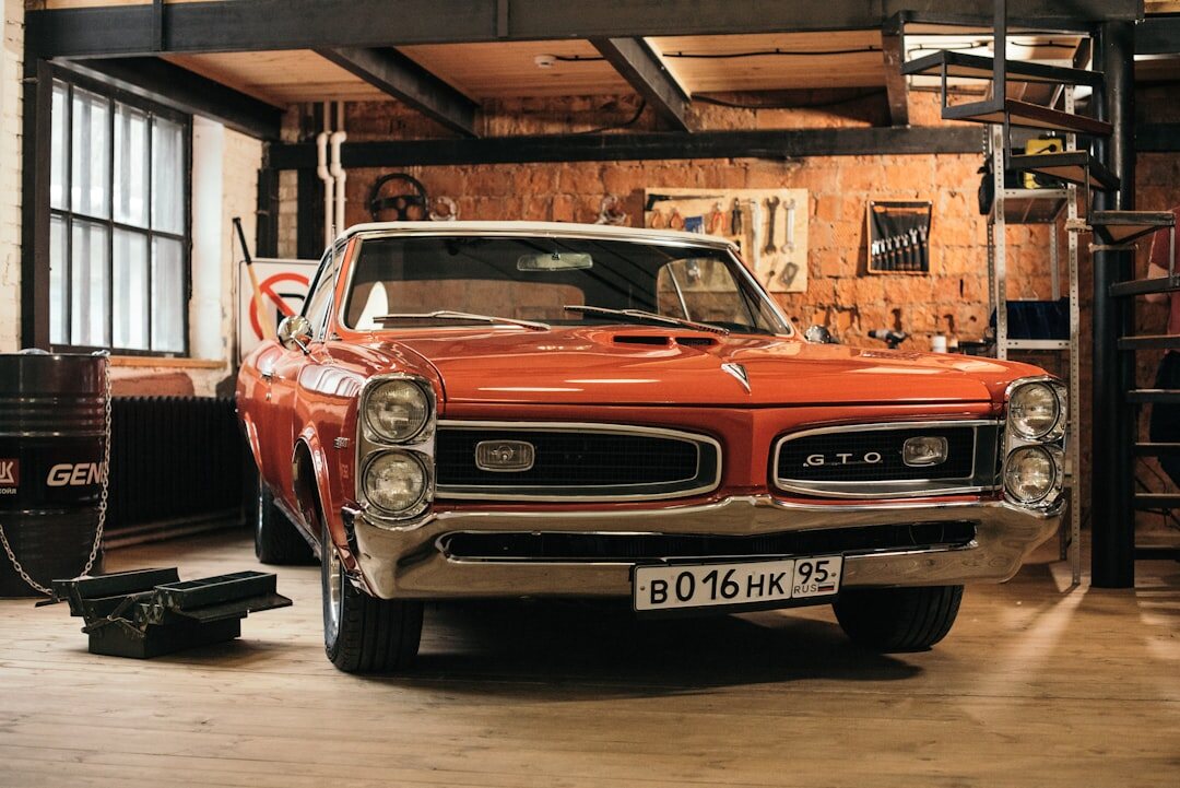 Elderly collector standing beside a restored classic automobile in a garage